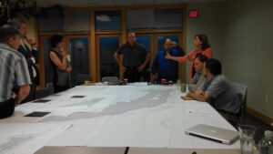 Members of the design team and conservancy discuss the design of the project around a large meeting table. A large printed site plan covers most of the table.