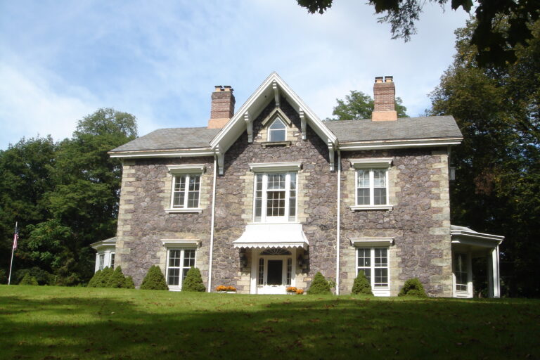 A photograph of the front of Willow Hall, a two-story house with attic, stone facade, and two chimneys.