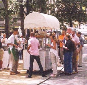 Older, grainy photograph showing people lining up at the park's hot dog cart.