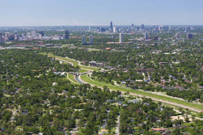 Aerial photo of a bayou channel through Houston with downtown visible in the distance.