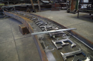 Photograph of the sign during fabrication. The metals looks raw and unpolished, and not all the letters are attached to the sign.
