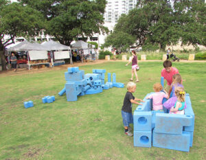 Children playing with large, light blue "Imagination Play" blocks on the lawn at the park.
