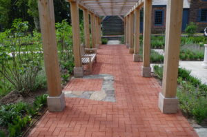 The stone outline of the historic privy is seen within the brick paving under the pergola.